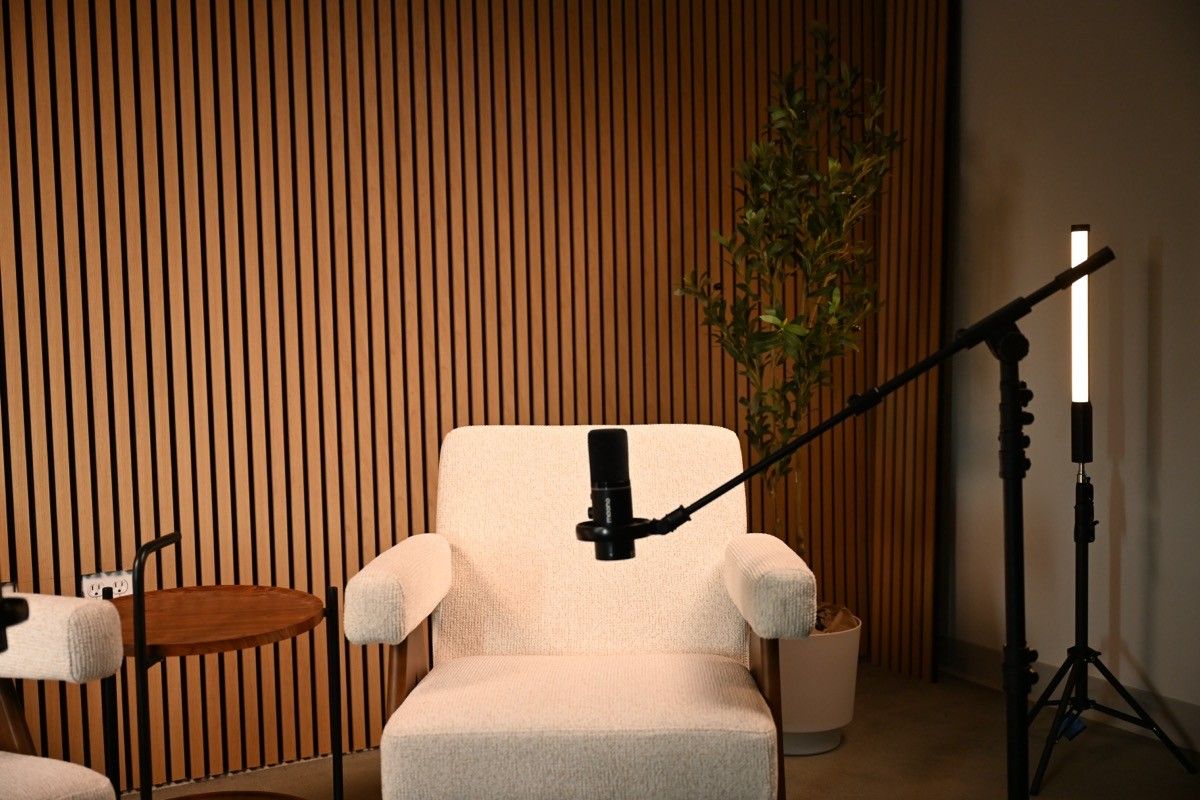 A cream chair with a boom microphone and a light stand in front of the slat wall at Axeom Content Studio